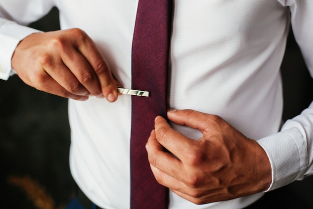 Lleva una camisa blanca con corbata roja. chico guapo con manos bien arregladas corrige su corbata de cerca.