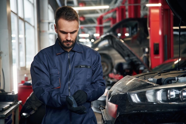 Llevando los guantes de pie el reparador de coches está en el garaje con el automóvil
