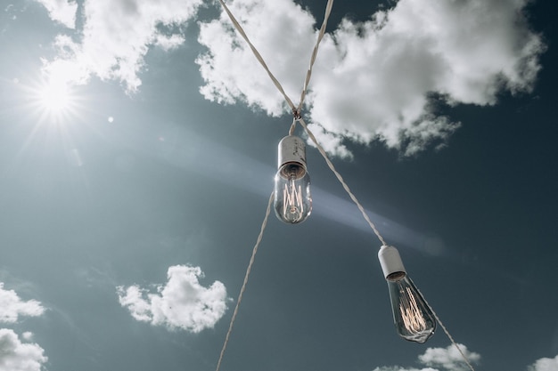 Llight bombillas en cables contra un cielo azul con el sol Luz del sol