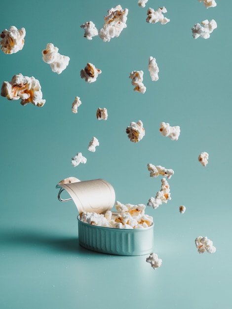 Lluvia de palomitas de maíz cayendo dentro de una lata o lata, aislado sobre fondo verde claro