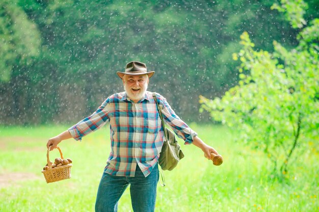 Lluvia de verano Anciano caminando Abuelo Pensionista Senior senderismo Setas en el bosque lluvioso Verano y pasatiempos