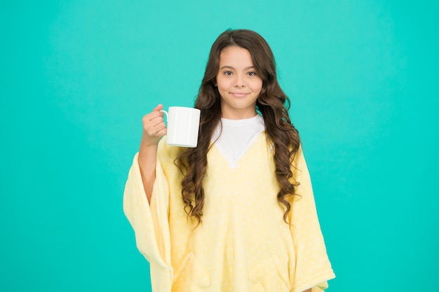 Lo mejor para beber en la mañana niña feliz con taza de té buenos días beber niño pequeño pared azul niña beber cacao o leche antes de dormir pijama acogedor y esponjoso sentirse cómodo en casa