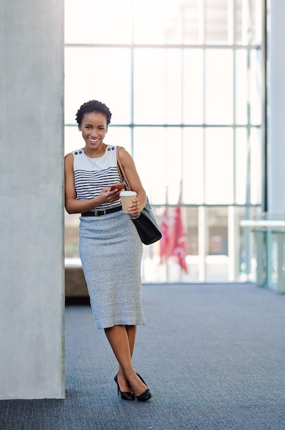 Lo único que atrae el éxito es la positividad Retrato completo de una atractiva joven empresaria sonriendo mientras usa un teléfono inteligente en una oficina moderna