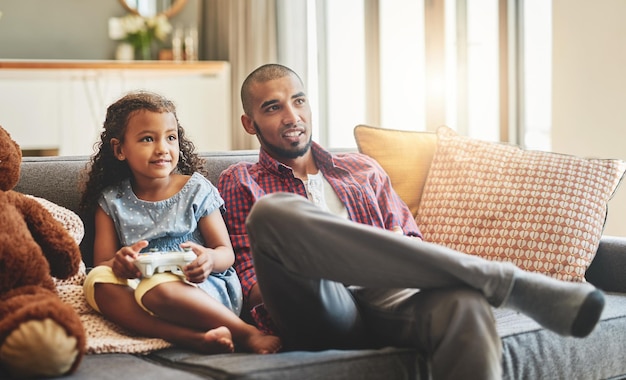 Lo único que no se puede pausar es el tiempo de vinculación Foto de una niña adorable y su padre jugando videojuegos juntos en el sofá de casa