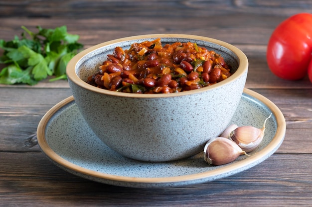 Lobio aus geschmorten roten Bohnen, Zwiebeln, Knoblauch, Gewürzen und Kräutern in einer Schüssel auf Holzhintergrund Nahaufnahme horizontal