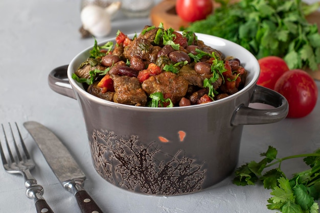 Lobio de estofado de ternera frijoles rojos cebollas ajo especias y tomates en un plato de cerámica sobre un fondo gris