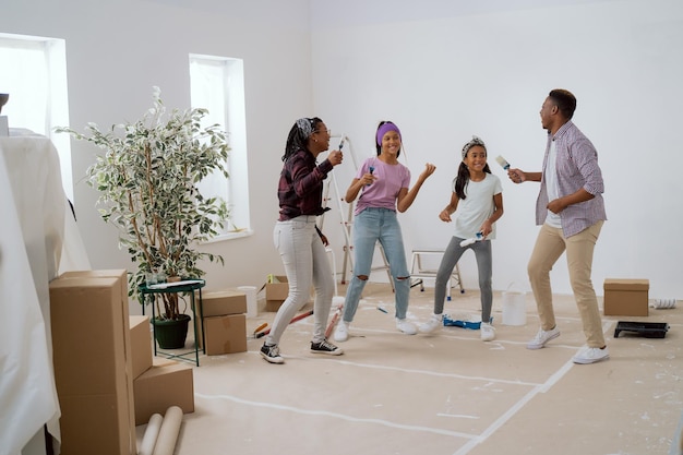 Loca familia feliz pintando las paredes con pintura blanca con pinceles bailan