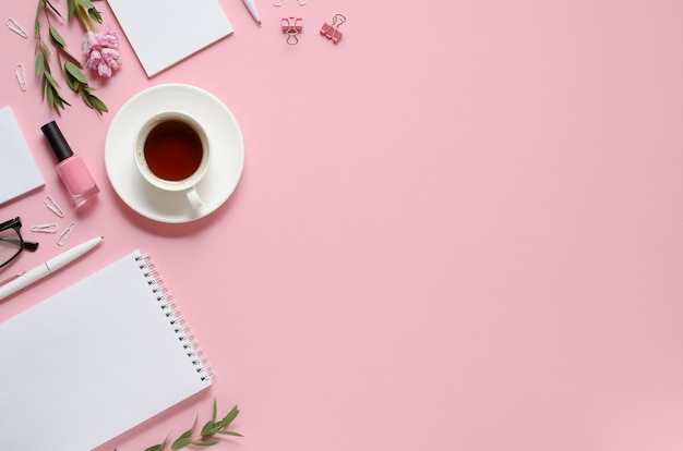 Local de trabalho com bloco de notas, caneta, xícara de café e outros acessórios em fundo rosa com espaço de cópia. vista do topo