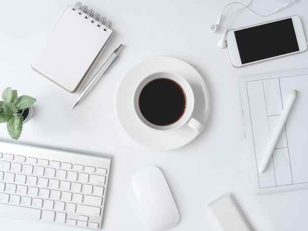 Local de trabalho com uma xícara de café, notebook, planta plástica, smartphone e teclado na mesa