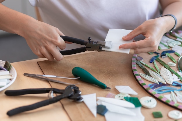 Local de trabalho das mãos das mulheres do mestre do mosaico segurando uma ferramenta para detalhes do mosaico no processo de fabricação ...