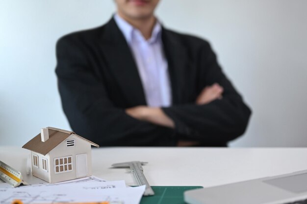 Foto local de trabalho de arquitetos com plantas de modelo de casa e suprimentos com arquiteto sentado em segundo plano