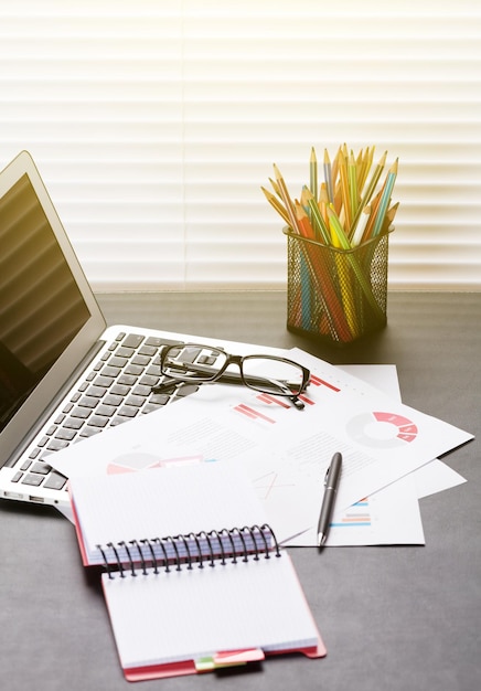 Local de trabalho de escritório com lápis e relatórios de laptop