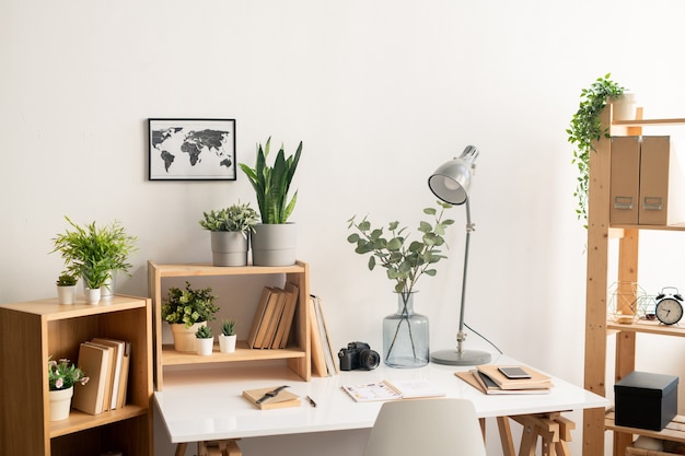 Local de trabalho de escritório com mesa com suprimentos, prateleiras de madeira com livros e vasos de flores e foto do mapa na parede