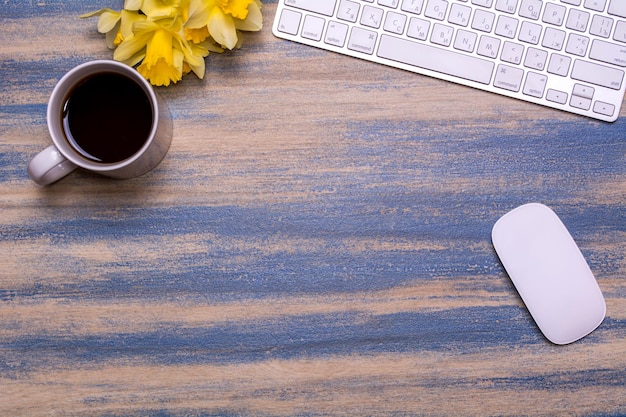 Local de trabalho de escritório com narcisos de teclado xícara de chá e mouse de computador em um fundo de madeira