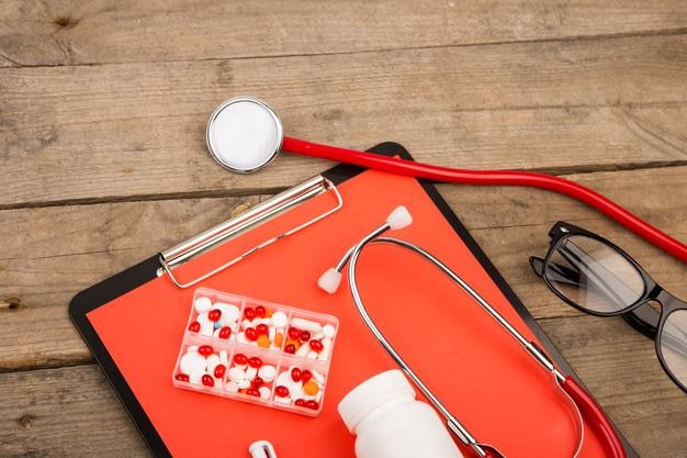 Local de trabalho de um médico Óculos de prancheta de estetoscópio e pílulas na mesa de madeira