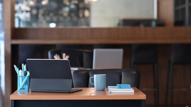 Local de trabalho do designer criativo com um computador tablet, xícara de café, caderno e artigos de papelaria na mesa de madeira.