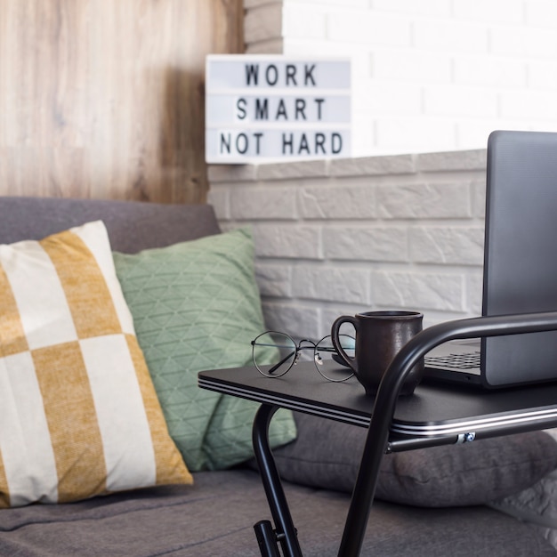 Local de trabalho em casa de um freelancer em uma mesa preta elegante perto do sofá e a parede de tijolo