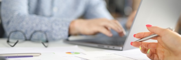 Local de trabalho no escritório, homem sentado atrás de laptop, mulher segurando a caneta sobre gráficos comerciais