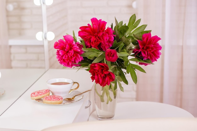 Local do cliente em um salão de beleza de cabeleireiro com uma xícara de donuts de chá e flores de peônias