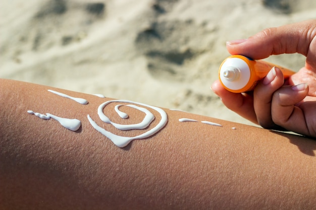 Loción solar para dibujar con protección solar en las piernas bronceadoras que relajan el bronceado en vacaciones en la playa tropical.