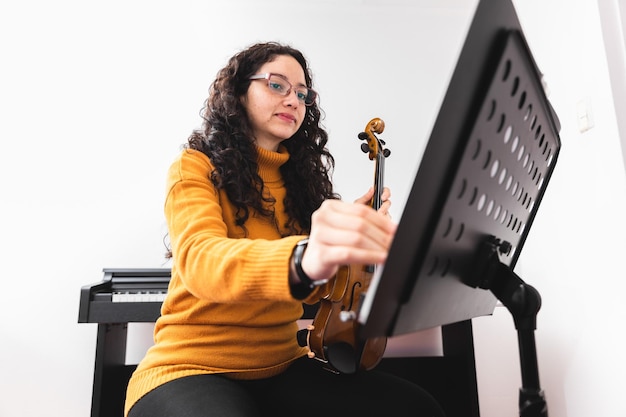 lockige brünette konzertfrau, die einen gelben pullover trägt, geige spielt und die blattmusikseite umblättert