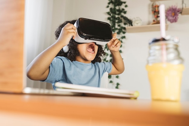 Lockiger Junge, der zu Hause eine Virtual-Reality-Brille spielt, überrascht, glücklicher offener Mund