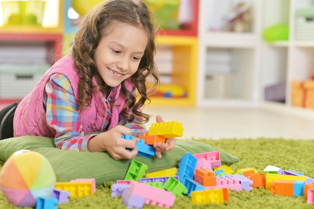 Lockiges kleines Mädchen, das mit bunten Plastikblöcken spielt