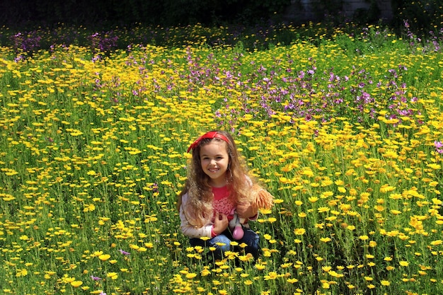 Lockiges kleines Mädchen mit einer roten Schleife im Haar Mädchen auf einer grünen Wiese zwischen gelben Blumen