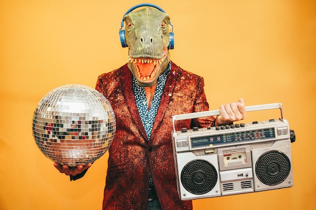 Foto loco con máscara de trex escuchando música con estéreo boombox vintage durante la víspera de año nuevo enfoque en la máscara