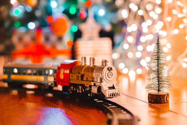 Foto locomotiva a vapor vintage de brinquedo no chão sob uma árvore de natal decorada em um fundo de guirlanda de luzes de bokeh