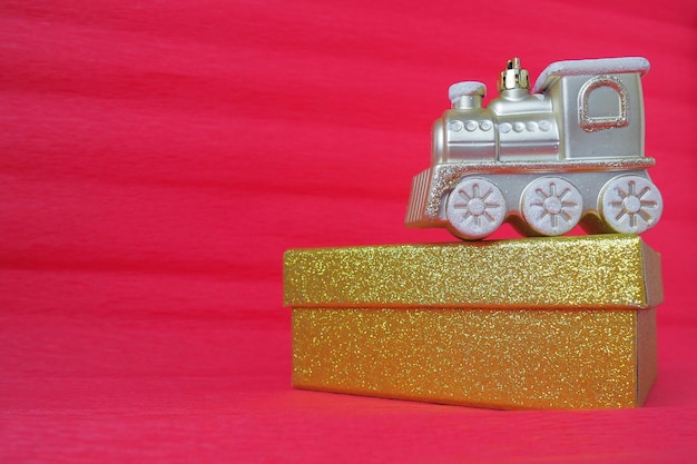 Locomotiva de trem de brinquedo dourado e caixa de presente de glitter em fundo gradiente vermelho e rosa Cartão de ano novo ou de Natal Pingentes e neve em um trem Espaço livre para texto Copiar espaço