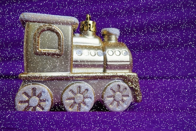 Locomotiva de trem de brinquedo dourado em um fundo gradiente roxo e lilás Cartão de ano novo ou de Natal Pingentes e neve no trem Espaço livre para texto Copiar espaço Bokeh de flocos de neve caindo festivos