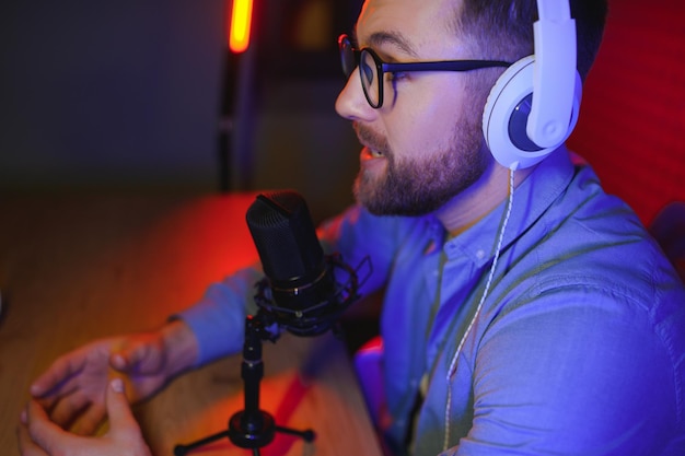 Locutor de radio masculino con auriculares en la cabeza y micrófono en el estudio leyendo noticias o programa de transmisión tonificado