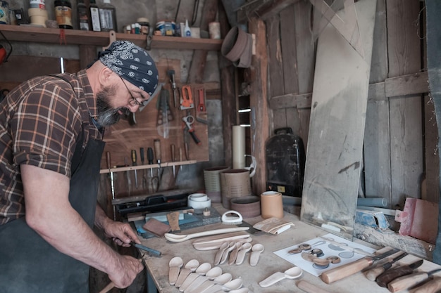 Löffelmeister in seiner Werkstatt mit Holzprodukten und Werkzeugen. Foto in hoher Qualität