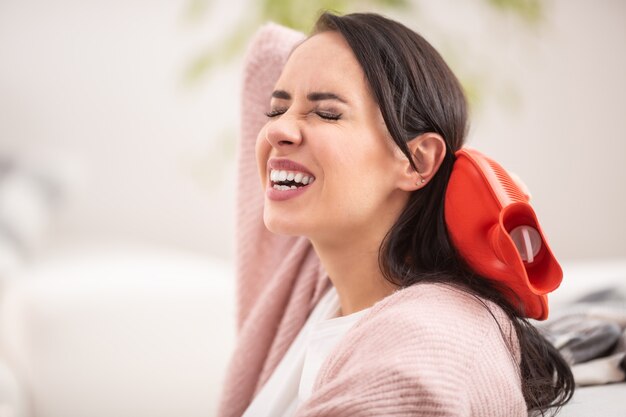 Lösen von Nackenschmerzen durch einen Thermophor einer brünetten Frau.