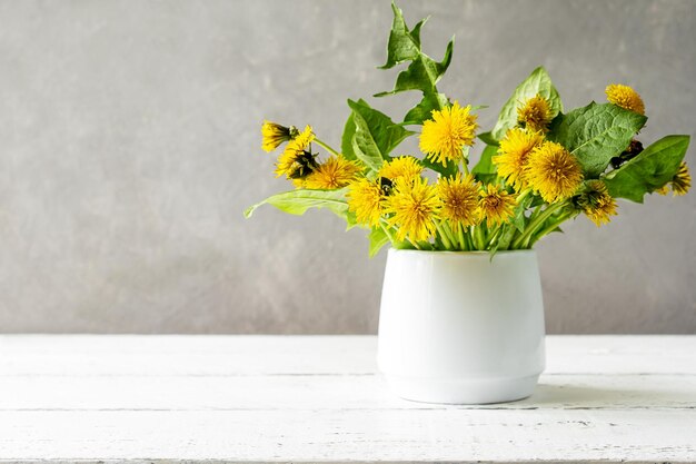 Löwenzahn in Vase auf weißem Holztisch mit Kopierbereich Gelbe, graue, weiße Farben