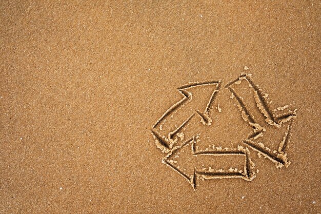 Logo des Recyclings auf Sand am Meeresufer