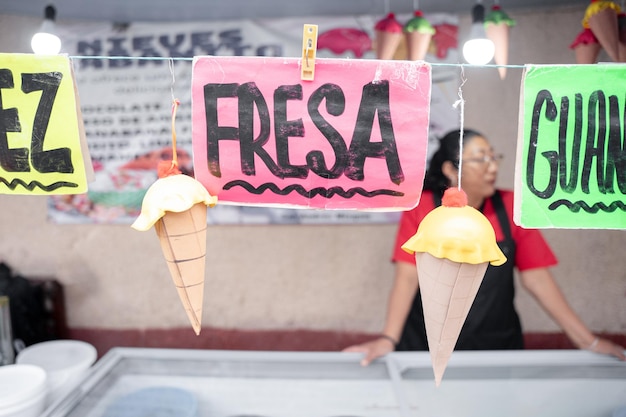 Foto logos de sabor a nuez y fresa en un puesto de helado en el mercado callejero con una mujer hispana en el fondo concepto de postre tradicional mexicano