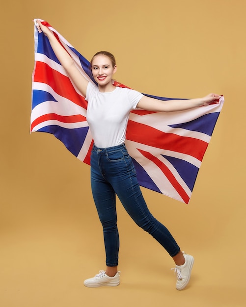 Loira atraente posa com uma bandeira britânica. sessão de fotos no estúdio em um fundo amarelo.