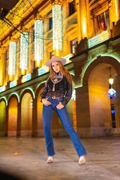 Loira caucasiana em jeans e uma jaqueta preta na cidade iluminada para o Natal à noite