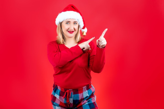 Loira com pijama de Natal em um fundo vermelho mostrando gestos com os dedos indicadores