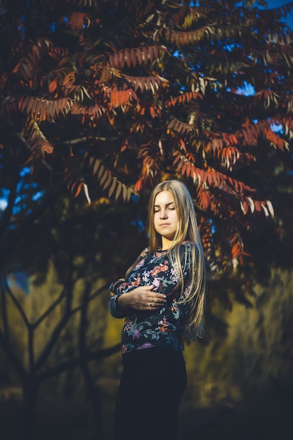 Loira de cabelos compridos de menina mulher em uma floresta com árvores com folhas vermelhas. Ela está feliz e confiante em uma sessão de fotos. Parque outono ensolarado dia quente. Conceito romântico.