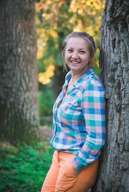 loira de calça laranja e camisa xadrez sorrindo na floresta