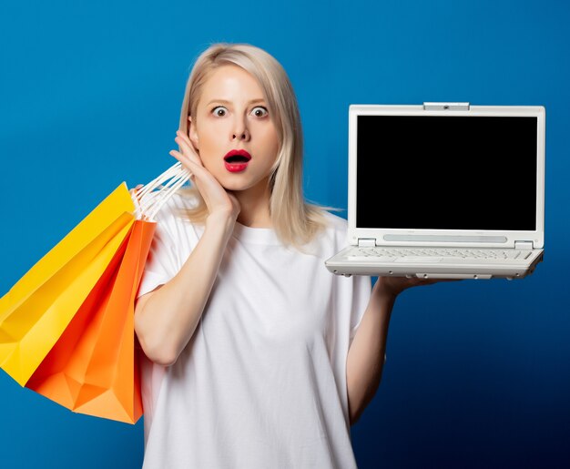 Foto loira em uma camiseta branca com sacolas de compras e um laptop no espaço azul