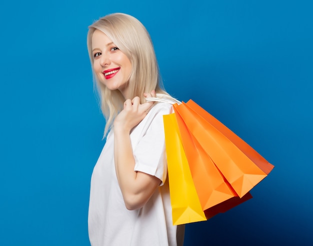 Loira em uma camiseta branca com sacolas de compras no espaço azul