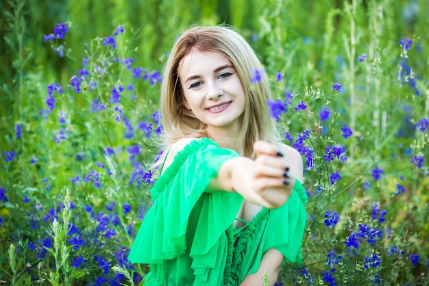 Loira europeia com um vestido verde na natureza com flores azuis