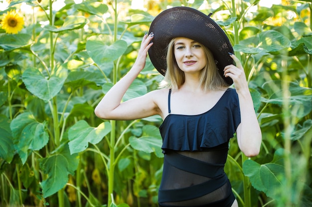 Loira européia em um maiô preto e chapéu na natureza com girassóis