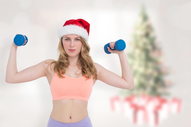 Loira festiva segurando halteres contra a árvore de natal embaçada no quarto