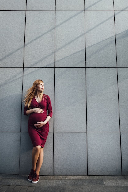 Loira garota grávida em um estilo casual. Na cidade grande. 9 meses esperando. Contra o pano de fundo do edifício de alta tecnologia.