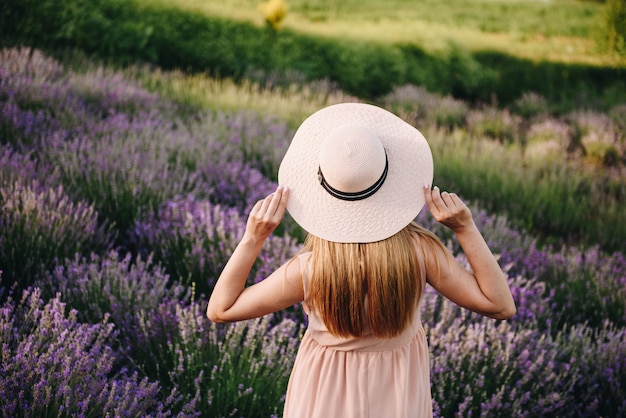 Loira garota grávida em um vestido bege e chapéu de palha. campo de lavanda. em antecipação de uma criança. a idéia de uma sessão de fotos. caminhe ao pôr do sol. futura mãe.